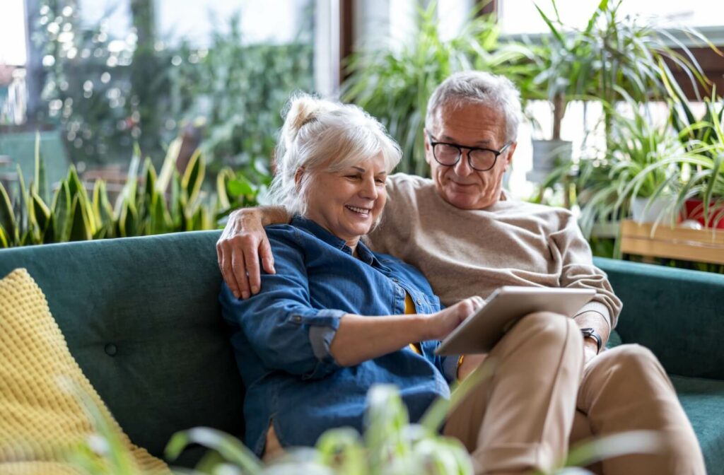 An older couple sitting on a couch looking at a tablet while researching senior living.