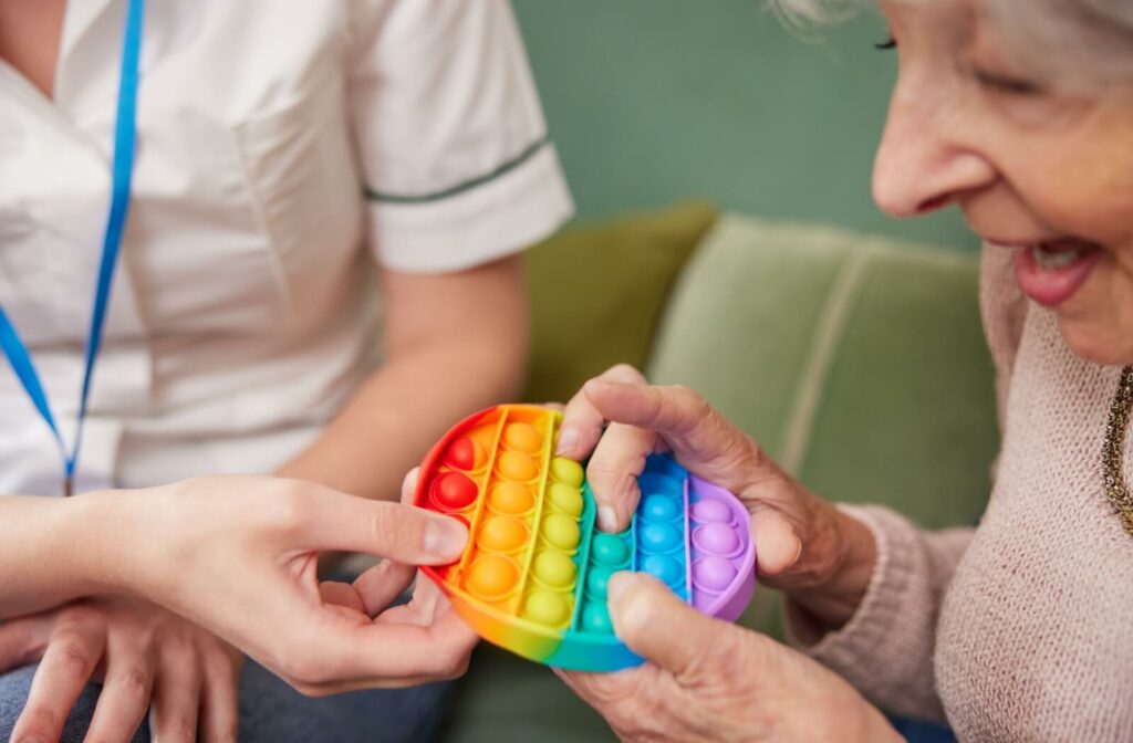 A caregiver offers a senior in memory care a rubber bubble toy to touch.