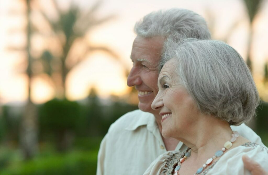 Younger adult supporting older adult outside in warm weather symbolizing caregiving and memory care in senior living community