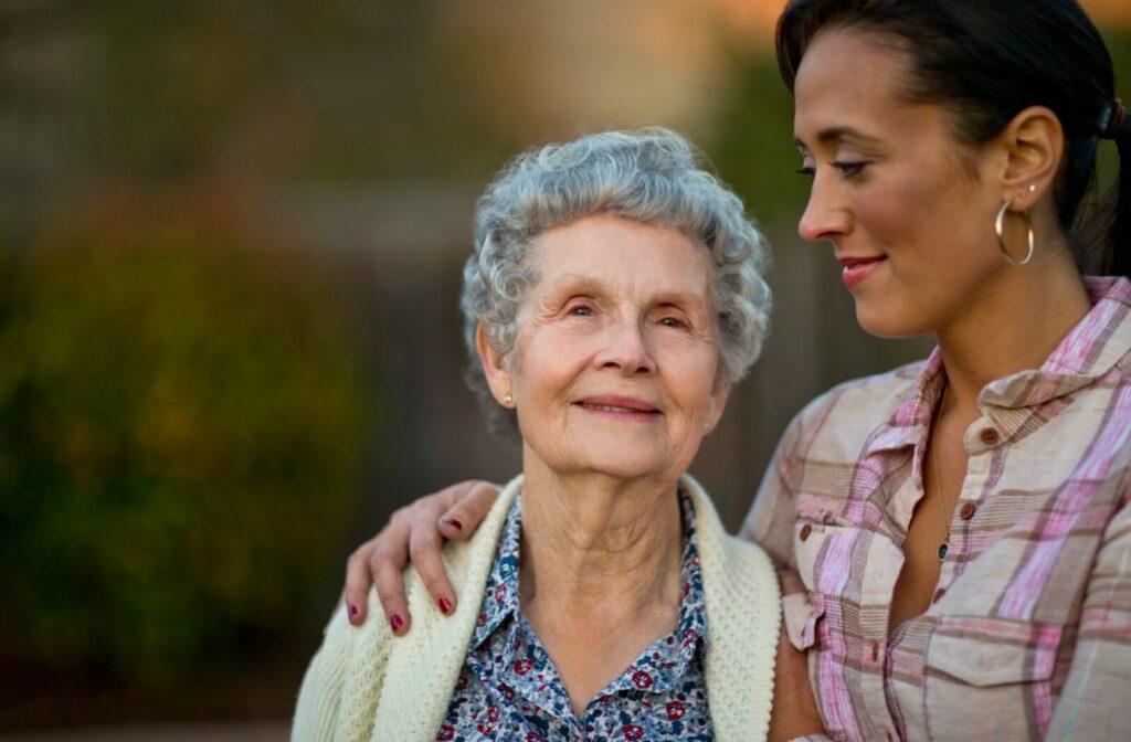 Younger adult supporting older adult outside in warm weather symbolizing caregiving and memory care in senior living community