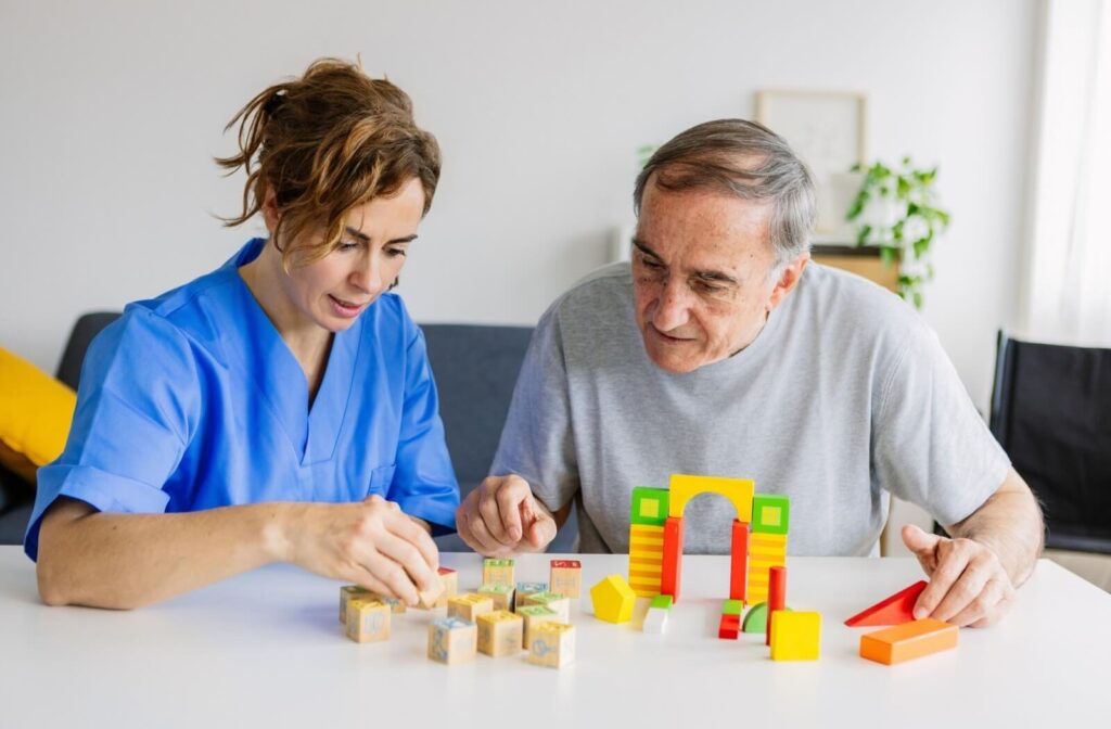caregiver in assisted living helps a smiling older adult stack wooden blocks and plastic toys to engage their memory in senior living