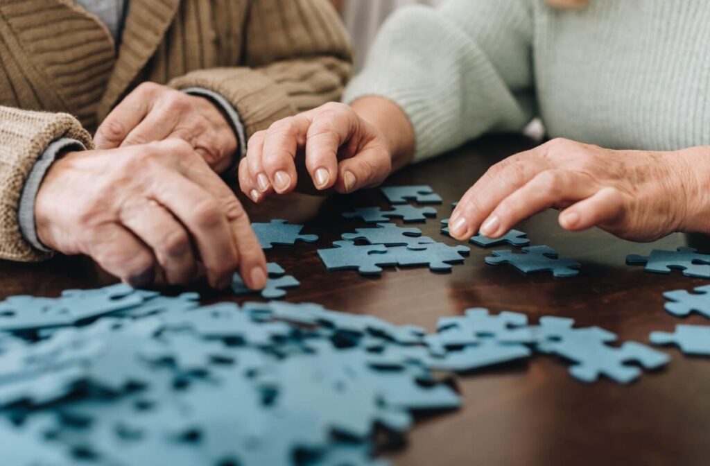 2 older adults work together to assemble a blue jigsaw puzzle on a wooden table in senior living