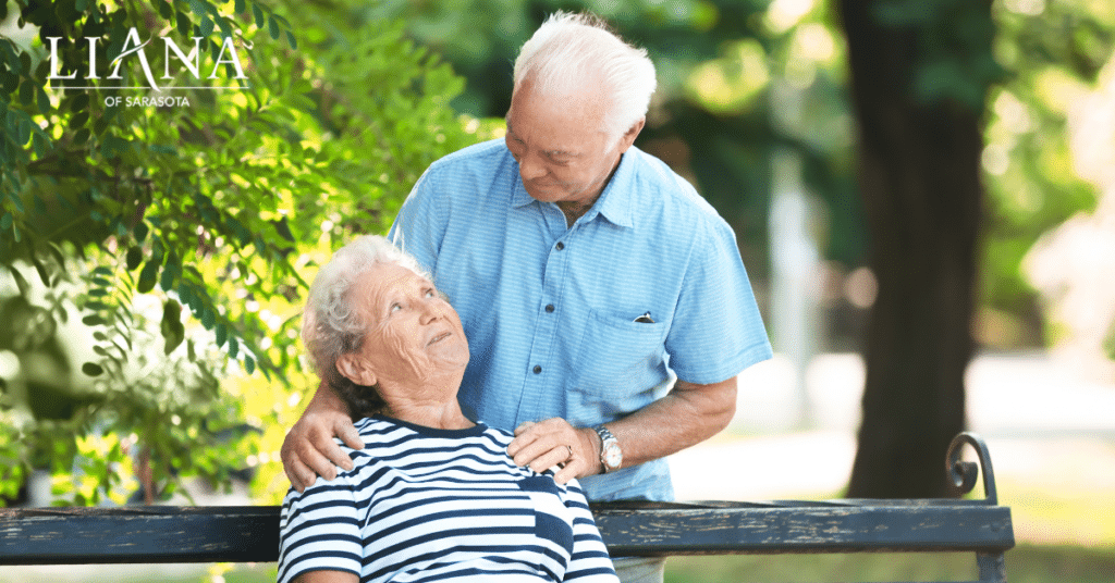 Older couple resting on a shaded park bench during hot weather while discussing senior living decisions.