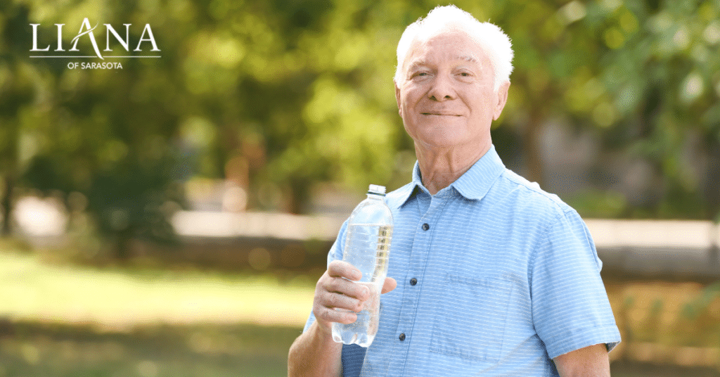 A smiling senior man drinking water outdoors during hot weather and staying hydrated while making senior living decisions.