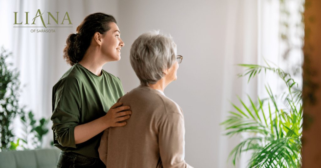 A care partner gently supports an older woman using a walker in a bright senior living space, showing comfort and care for someone who may live in hospice.