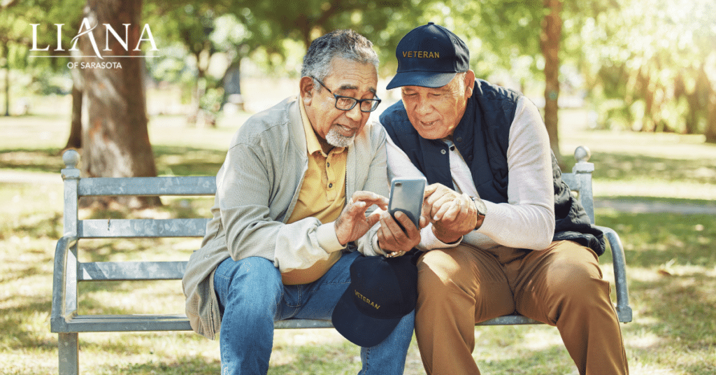 Two senior men sharing photos on a smartphone while sitting outdoors and choosing a memory care community.