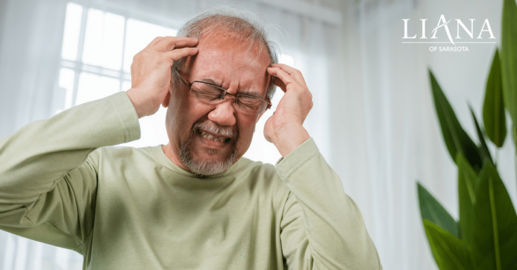 An older man holding his head in distress at home, illustrating difficult behaviors and emotional challenges addressed in senior memory care.